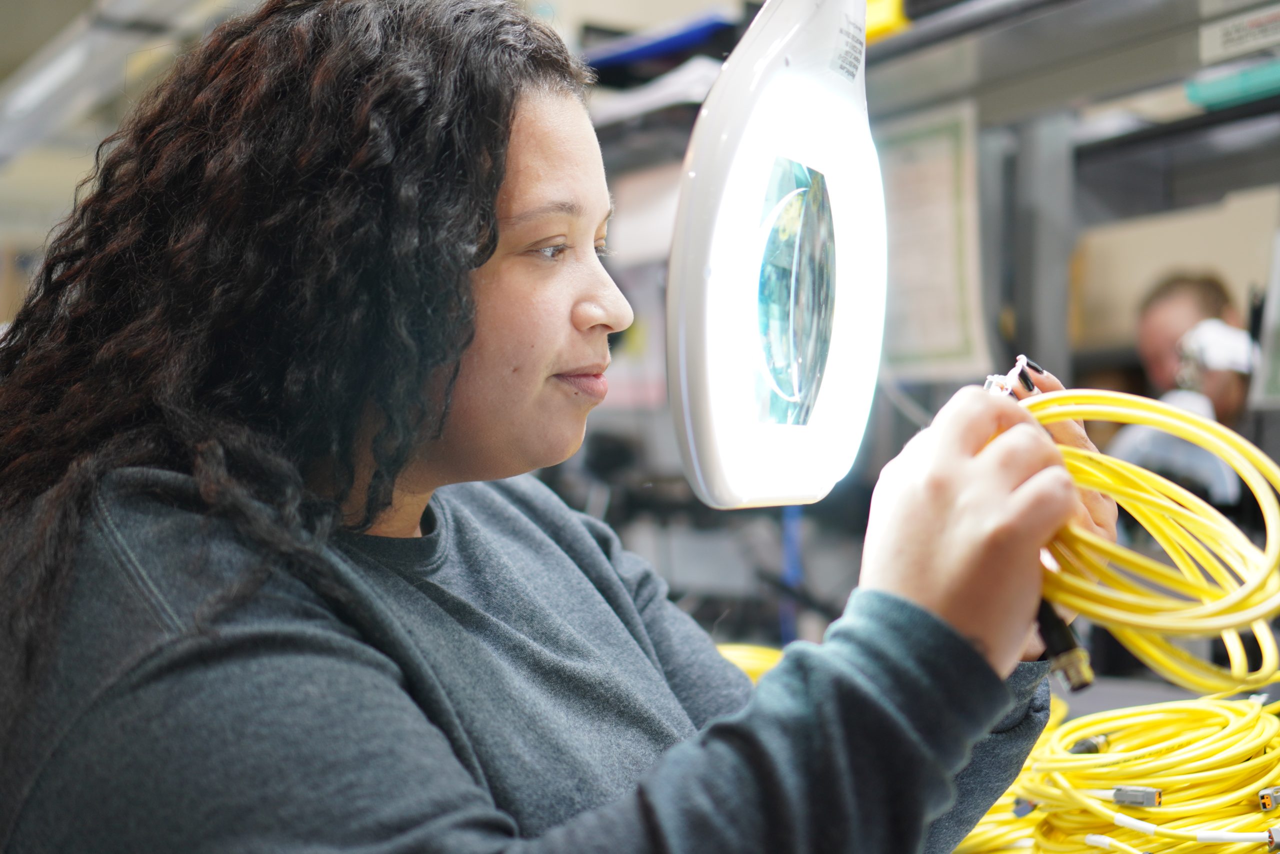 A female employee holds a yellow bundle of cable as she checks for quality.