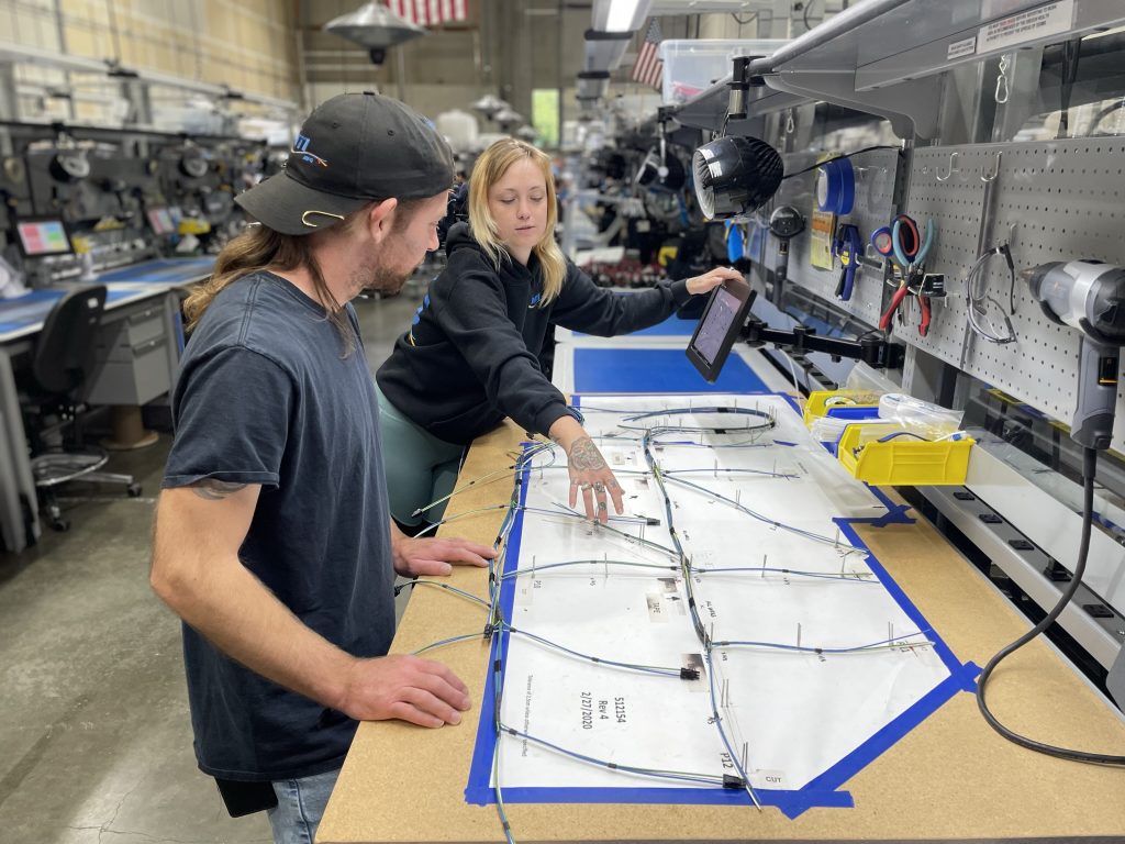 Two employees work on a cable assembly together