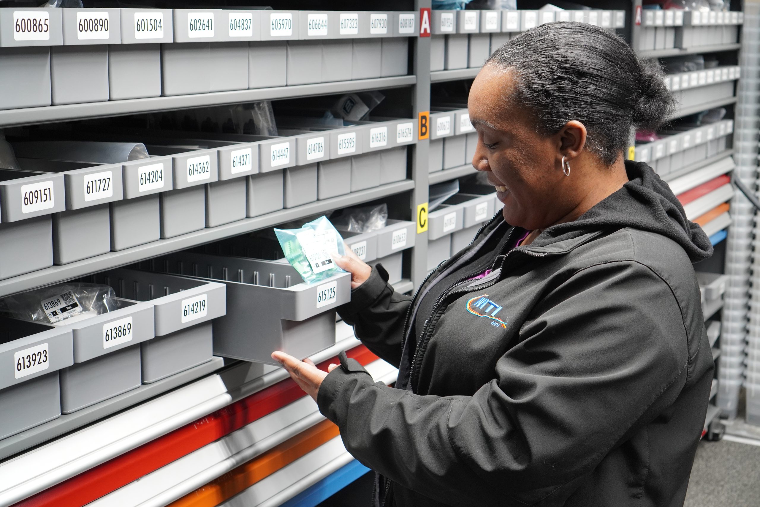 A female employee smiles as she picks out an item from an inventory shelf.