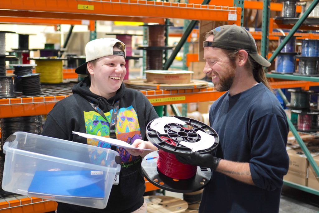 Two employees at Multi-Tek smile as they hold material