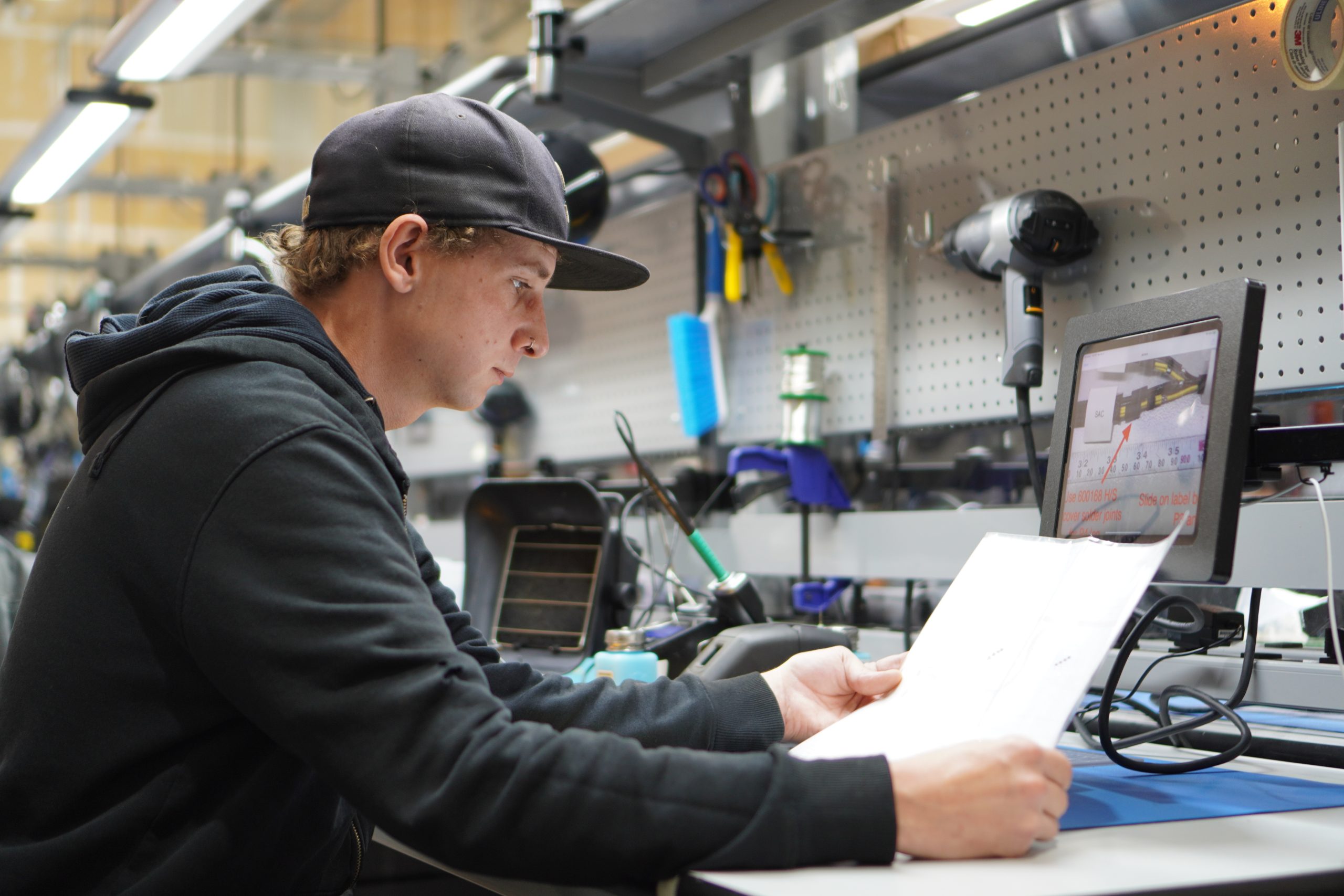 A male employee consults a visual design on screen and on paper to double-check his work.